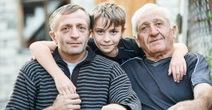 Multi generation portrait of happy grandfather with his son and grandson sitting in front of the country house; blog: Is Degenerative Disc Disease Genetic?