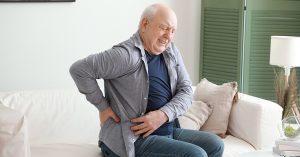 Senior man suffering from back pain at home; blog: Does Cold Weather Cause Back Pain?
